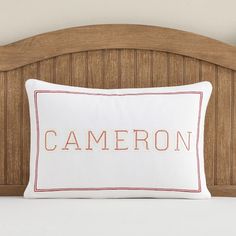 a white pillow with the word cameron on it sitting in front of a wooden headboard