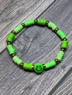 Smiley face bracelet with different colors of green. Smiley face charm in the center. Tie closure, stretchy material. One size fits most. Trendy Cheap Stretch Bracelet With Smiley Face, Cheap Trendy Stretch Bracelet With Smiley Face, Cheap Novelty Green Beaded Bracelets, Cheap Green Novelty Bracelets, Different Colors Of Green, Green Smiley Face, Smiley Face Bracelet, Colors Of Green, Smiley Face