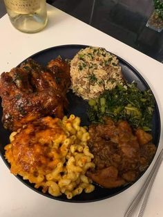 a black plate topped with meat, pasta and veggies next to a bottle of wine