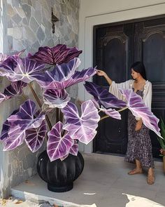 a woman standing in front of a black vase filled with purple flowers next to a door