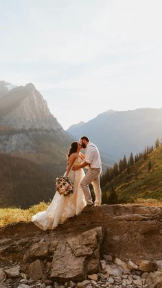 a bride and groom standing on top of a rock wall with mountains in the background