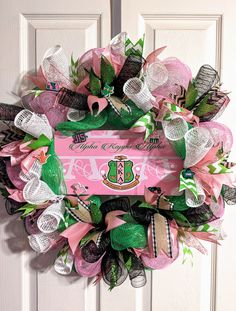 a pink and green wreath on the front door is decorated with ribbons, bows and personalized nameplates