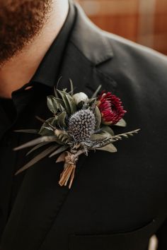 a man wearing a black suit and red flower boutonniere on his lapel