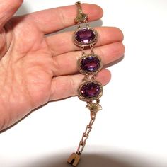 A 1940's Egyptian Revival tested 14 K rose gold retro Synthetic Alexandrite bracelet. The handmade bracelet consists of a box clasp, and three central ovals with fancy frames set with three large oval Synthetic Alexandrites. The stones are framed by a pair of lotus blossoms, and a short length of chain leads to the clasp. The bracelet has Arabic hallmarks on the clasp, and faint Arabic hallmarks on the back of each central oval and the lotus blossoms. The bracelet is in excellent condition with no obvious signs of wear. There are a very few very small chips to the facets on the undersides of the stones, but none on the top. The bracelet measures 17.5 cm, with the central section measuring 10.4 cm from the end of one lotus blossom to the end of the other. The stones measure 1.7 by 1.2 cm. T Vintage Formal Bracelet With Box Clasp, Antique Rose Gold Bracelets For Formal Occasions, Heirloom Metal Bracelets For Formal Occasions, Heirloom Style Metal Bracelets For Formal Occasions, Formal Oval Costume Jewelry Bracelets, Vintage Rose Gold Bracelets For Gift, Vintage Rose Gold Bracelet For Gift, Formal Oval Costume Jewelry Bracelet, Vintage Rose Gold Bracelet Gift