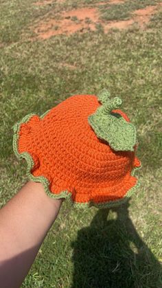 a hand holding an orange crocheted hat with a green leaf on the top