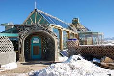 a building made out of rocks with a blue door in the middle and snow on the ground