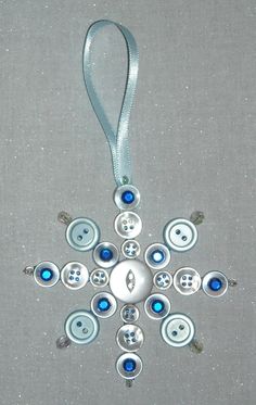 a snowflake ornament made out of buttons on a gray background with a silver ribbon