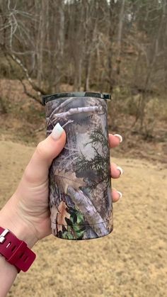 a woman holding up a camo coffee cup in her hand with trees in the background