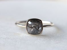 a gray diamond ring sitting on top of a white surface with the stone in it's center