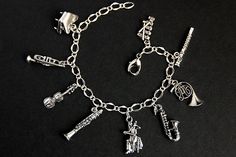 A collection of silver plated musical instrument charms have been dispersed around a shimmering silver plated bracelet chain in this handmade charm bracelet. This orchestra charm bracelet is then completed with a lobster clasp and a 1/2 inch of chain at the end for adjustable sizing. Charms in this bracelet include a piano charm, trumpet charm, violin charm, clarinet charm, cellist charm, saxophone charm, French horn charm, flute charm, and xylophone charm. ● Sizing ● To determine your bracelet Music-themed Silver Metal Jewelry, Silver Music-themed Metal Jewelry, Music-themed Band Jewelry As Gift, Music-themed Band Jewelry Gift, Music-themed Bracelet Jewelry Gift, Adjustable Silver Music-themed Bracelets, Adjustable Silver Music-themed Bracelet, Silver Metal Band Jewelry, Silver Band Jewelry In Metal