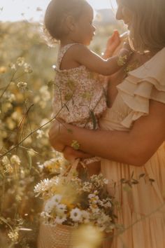 a woman holding a child in her arms while standing in a field full of flowers