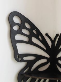 a black butterfly shaped metal object mounted on a white wall next to a shelf with a clock