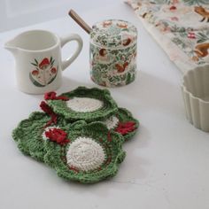 crocheted coasters and mug holders on a white table with christmas themed napkins