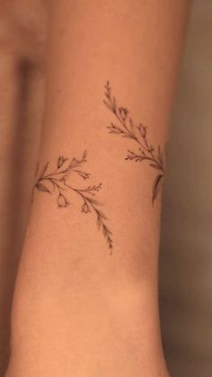 a woman's arm with a small branch tattoo on the left side of her wrist