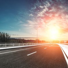 an empty highway with the sun setting in the background and clouds above it on a clear day