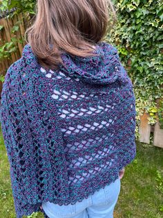 a woman wearing a blue crocheted shawl standing in front of a fence