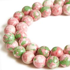 pink and green marble beads are arranged in a circle on a white surface with one bead facing the camera