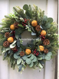 a wreath with pine cones, berries and greenery is hanging on the front door