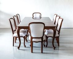 a dining room table and chairs with white upholstered backrests in an empty room