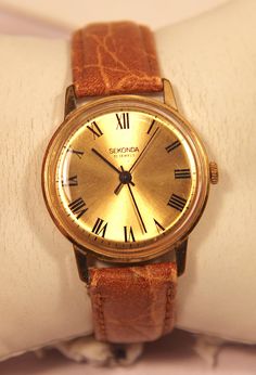 This vintage mens sekonda watch has a very reliable manual wind eastern european movement that has 19 jewels. A lovely clean gold dial with black roman numerals and all three hands (minute, hour and seconds) are also black. A men's dress/formal watch has a gold plated casing with a brown leather two piece strap. On the edge of the casing there is a marking stating 'AU 10' this would indicate the casing is gold plated. This watch comes with a lovely (rich brown) textured leather strap which shows Formal Watch, Sekonda Watch, Three Hands, Eastern European, Dress Formal, Eastern Europe, Wristwatch Men, Roman Numerals, Mechanical Watch