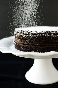 a chocolate cake is sprinkled with powdered sugar on a white platter