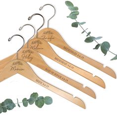 three wooden hangers with personalized names on them and green leaves hanging from the hooks