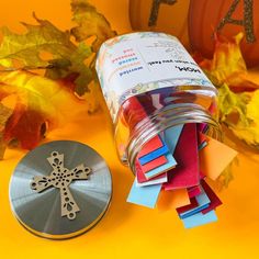 a jar filled with lots of different colored paper next to a metal cross on top of a table