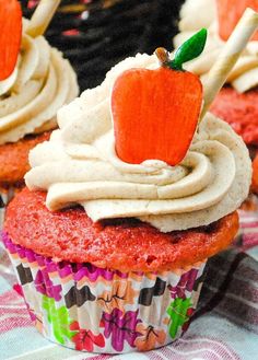 cupcakes with white frosting and an orange apple on top are sitting on a table