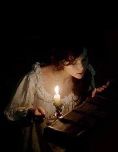 a woman sitting at a table with a lit candle in her hand and looking down