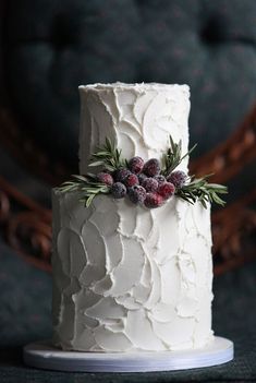 a white frosted cake with cranberries and greenery on top, sitting on a table