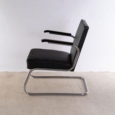 a black leather chair sitting on top of a white floor next to a metal frame