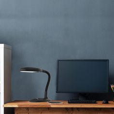 a desk with a monitor, keyboard and pencils on it in front of a gray wall