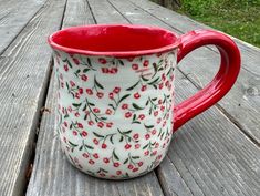 a red and white flowered mug sitting on top of a wooden table next to grass