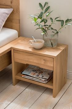 a small wooden table with a bowl on it next to a bed and plant in the corner