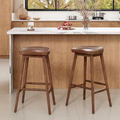 two wooden stools sit in front of an island with marble countertops and windows