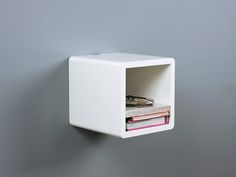 a white cube shaped shelf with books and magazines in it on a gray wall next to a grey wall