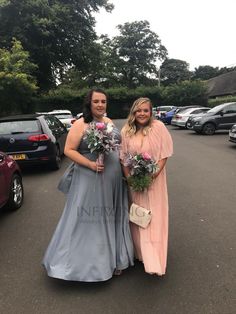 two women standing next to each other on a parking lot with cars in the background