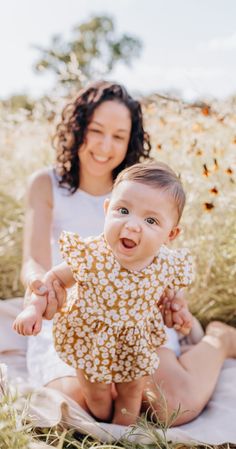 a woman sitting on the ground holding a baby's hand in front of her