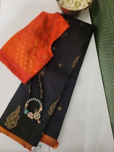 Black Kancheepuram silk saree with orange selvedge. The saree has tiny and large flower gold zari motifs all over the body and the pallu has traditional kattam buttis and Mayil patterns in gold zari. The blouse is black Kanchipuram silk with orange selvedge. This silk saree gives a stunning woven pattern, a masterpiece of artistry and craftsmanship. Draped in this, you will exude timeless charm and sophistication. South Indian Saree, Saree Outfits, Blouse Tutorial, Embroidery Sarees