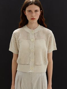 a woman standing in front of a black background wearing a white shirt and beige shorts