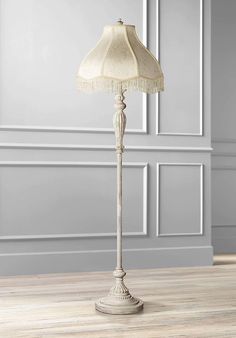 a floor lamp with a white shade on it in an empty living room, against a gray wall