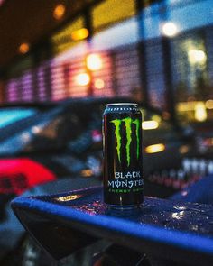 a can of monster energy drink sitting on top of a table in front of parked cars