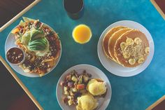 three plates of food on a blue tray next to a glass of orange juice and some pancakes