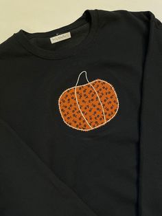 This charcoal sweatshirt is a unisex with a hand embroidered pumpkin in fabric applique on the front chest area. Orange with black floral pumpkin. Black Tops With Embroidered Graphics For Fall, Black Embroidered Tops For Fall, Casual Embroidered Sweatshirt For Fall, Black Embroidered Sweater For Fall, Black Cotton Sweatshirt For Fall, Fall Cotton Sweatshirt With Embroidered Patch, Long Sleeve Tops With Embroidered Patch For Fall, Black Cotton Sweater With Embroidered Graphics, Fall Sweatshirt With Embroidered Graphics