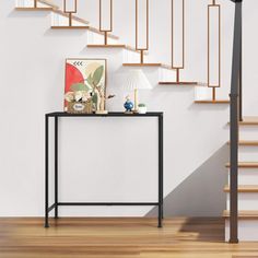 a table with a lamp and pictures on it next to a stair case in a white room