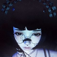 a woman with black hair and white face paint is wearing a blue nose ring while standing in front of a dark background