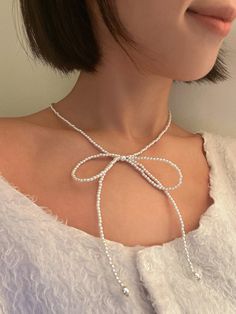 a woman wearing a white necklace with pearls and a bow on the back of her neck