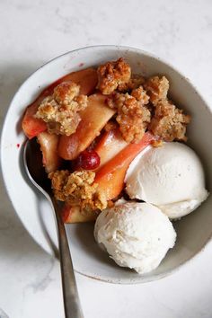 a bowl filled with fruit and ice cream on top of a white table next to a spoon