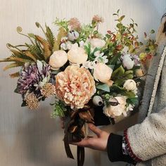 a woman holding a bouquet of flowers in front of a wall with a white background