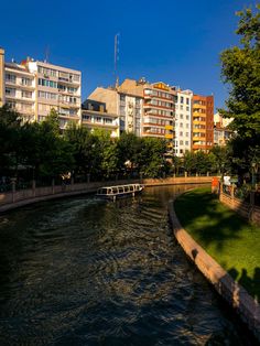 a river running through a city with tall buildings on both sides and green grass in the foreground